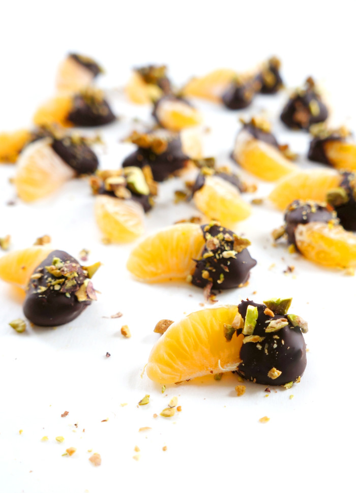 Closeup of chocolate-Dipped clementines with chopped pistachios on a white surface
