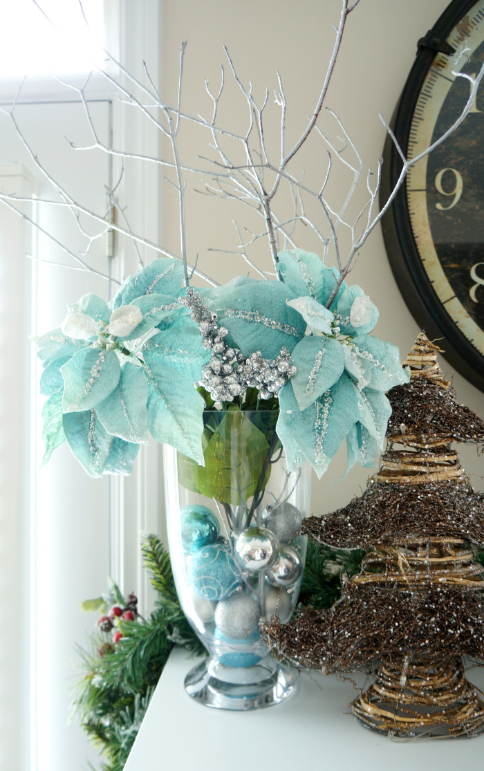 Blue flowers and silver branches in a clear vase filled with blue and silver ornaments