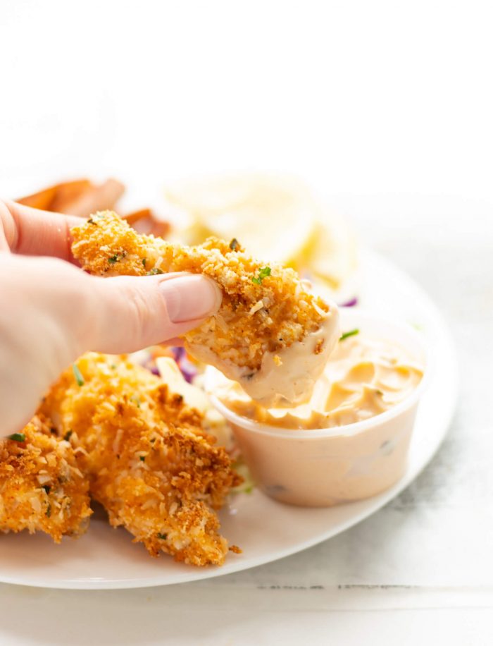 Almond Coconut Crusted Fish Sticks being dipped in roasted garlic spread