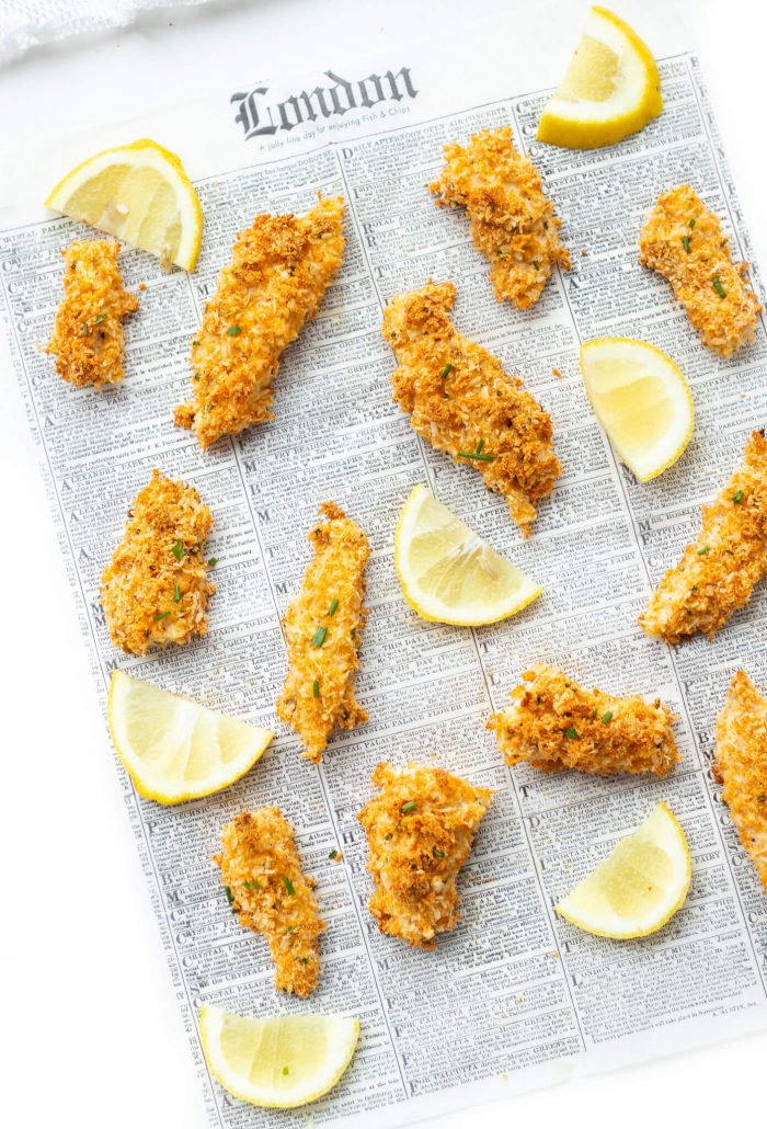 Overhead shot of Almond Coconut Crusted Fish Sticks and lemon slices on a newspaper