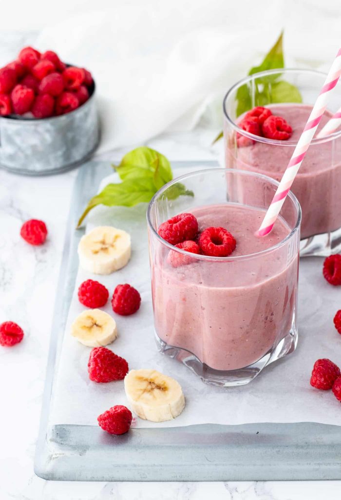 raspberry protein shake in glasses with fresh bananas and raspberries