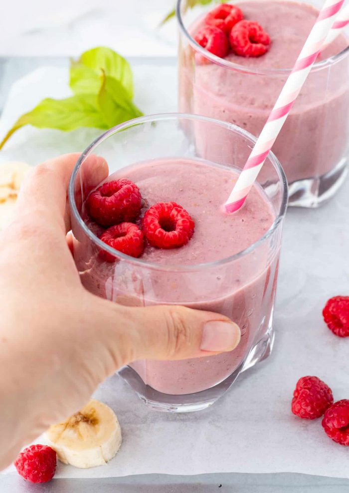 holding raspberry protein shake in glass with straw