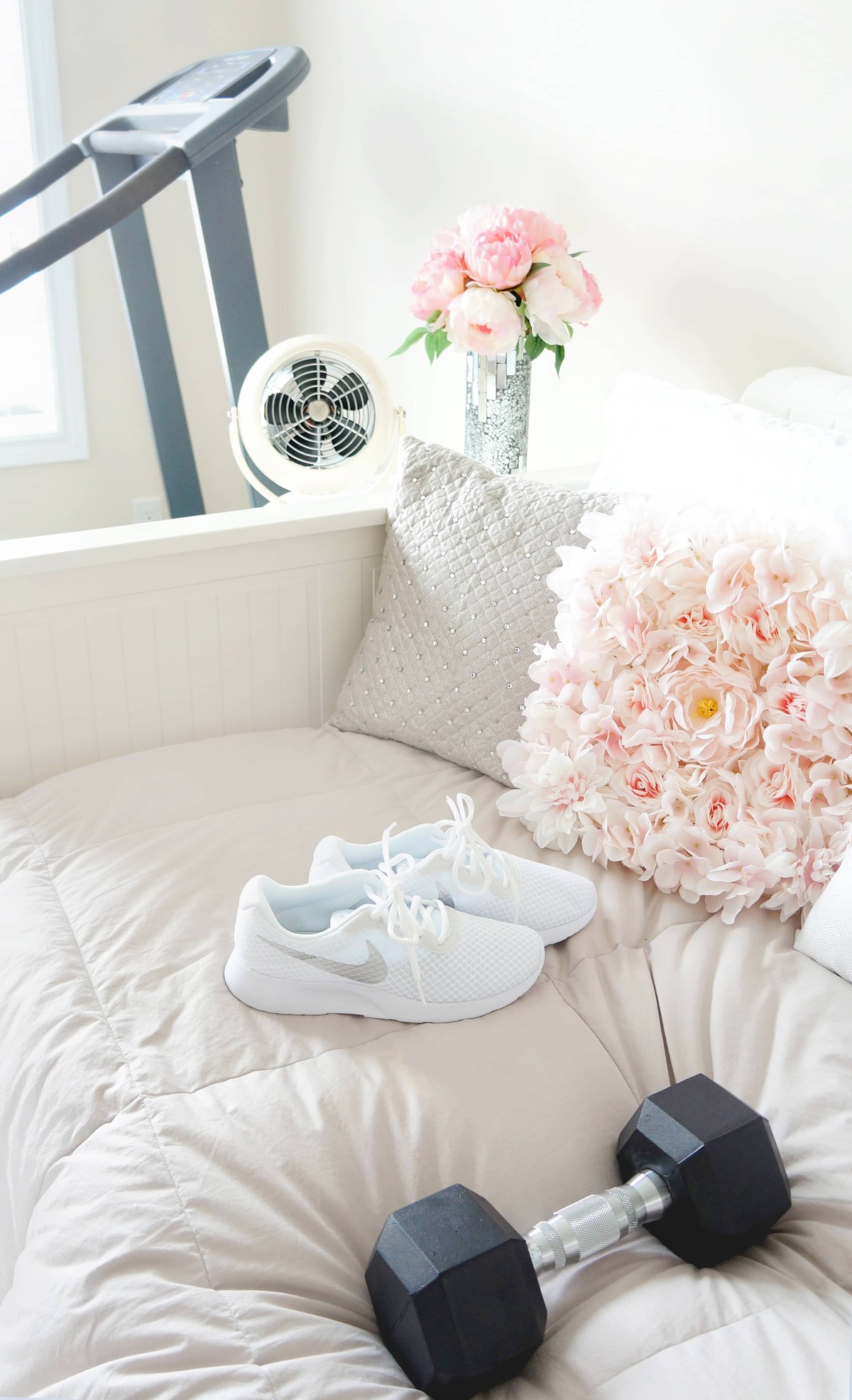 White workout shoes next to a dumbbell and a pink flower pillow