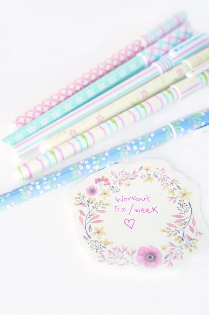 Colorful pastel pens and a floral piece of paper that reads \"Workout 5x/week\" with a heart