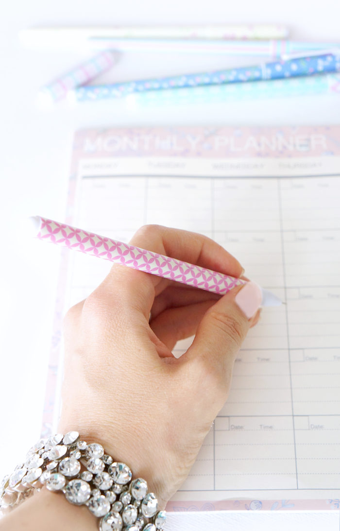 Hand holding a pink pen over a monthly planner