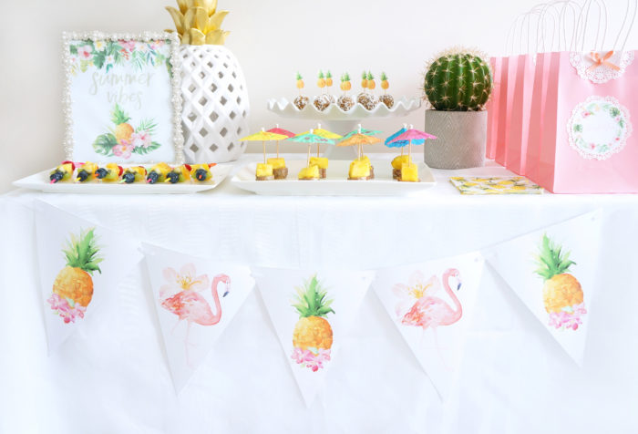 Banner with flamingos and pineapples hanging from a table full of tropical foods and decorations