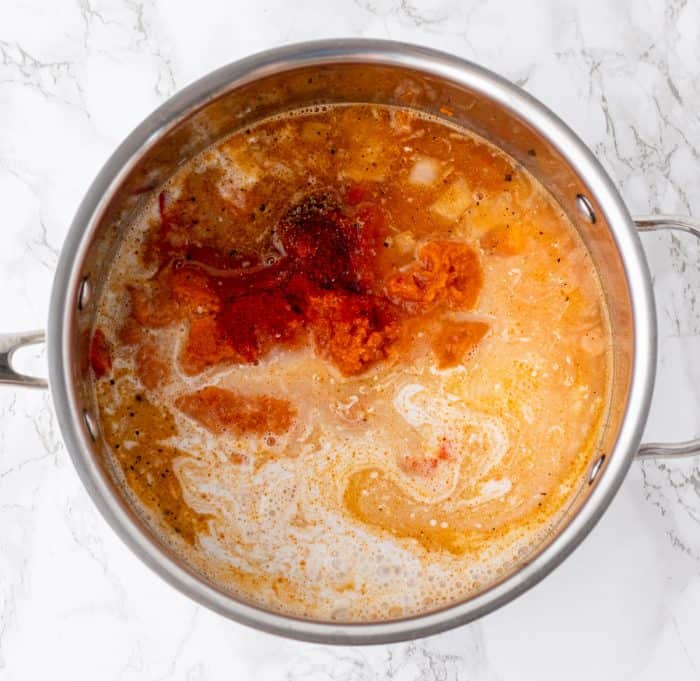 coconut milk, spices, pumpkin and red curry paste cooking in a large sauce pan on marble background