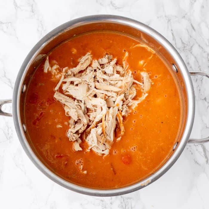 shredded chicken added into curried pumpkin soup in a large sauce pan on marble background