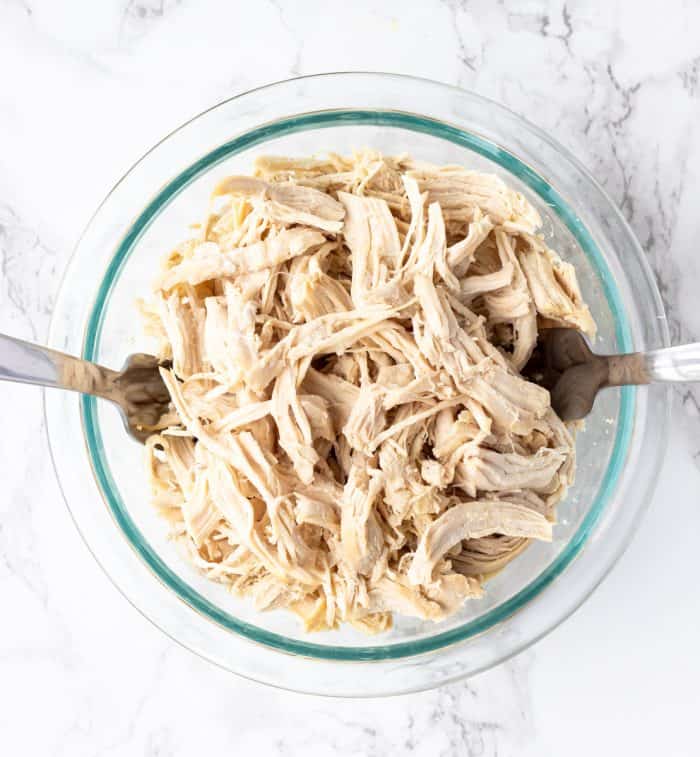 a bowl of shredded chicken with two forks on marble background