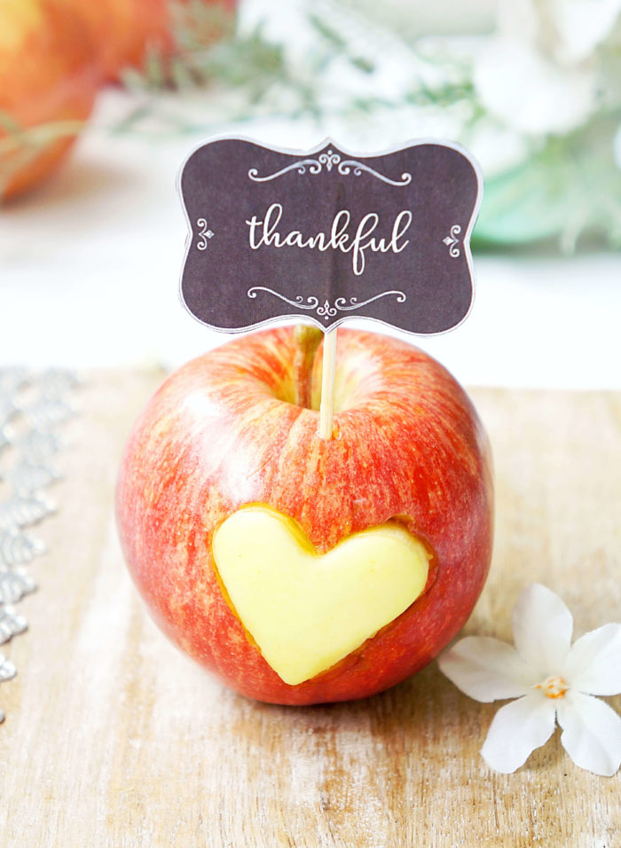 Red apple with a yellow heart in it and a toothpick that says \"thankful\" in script