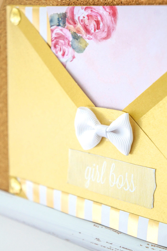 Golden envelope with words \"Girl boss\" decorated with a white bow and filled with floral paper