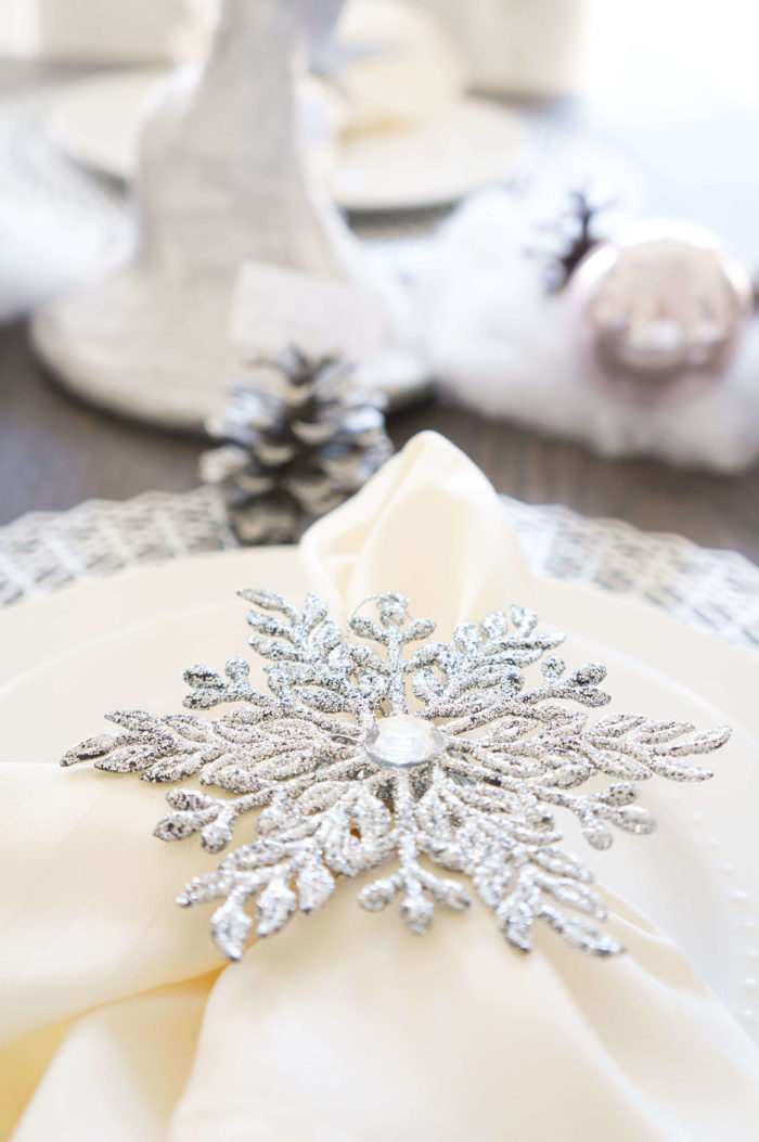 Closeup of silver snowflake napkin ring around an ivory napkin on a white dish