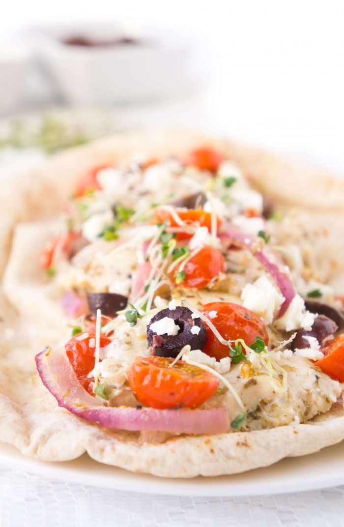 Line of pitas topped with Greek Chicken & Veggies, olives, and toppings