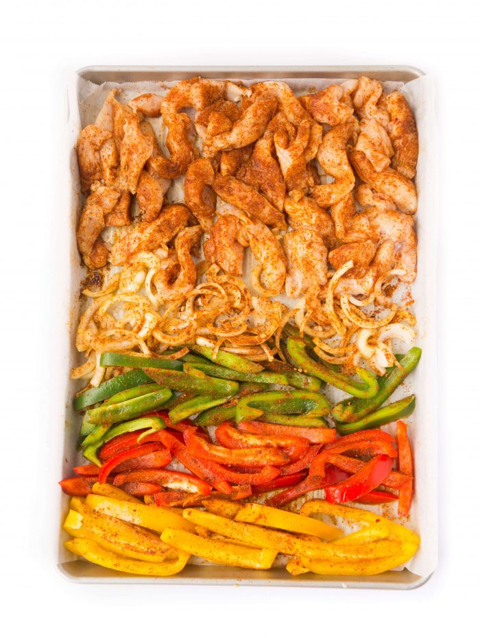 Seasoned chicken, onions, and bell peppers on a sheet pan
