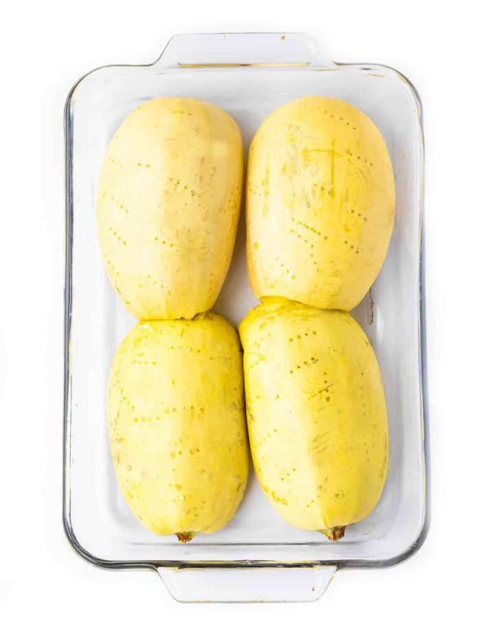 Four spaghetti squash halves face down in a large glass baking dish on a white background