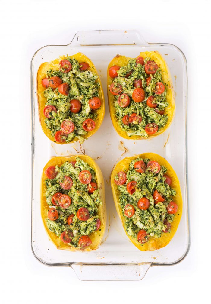 Pesto chicken and diced tomatoes stuffed in spaghetti squash halves in a glass baking dish