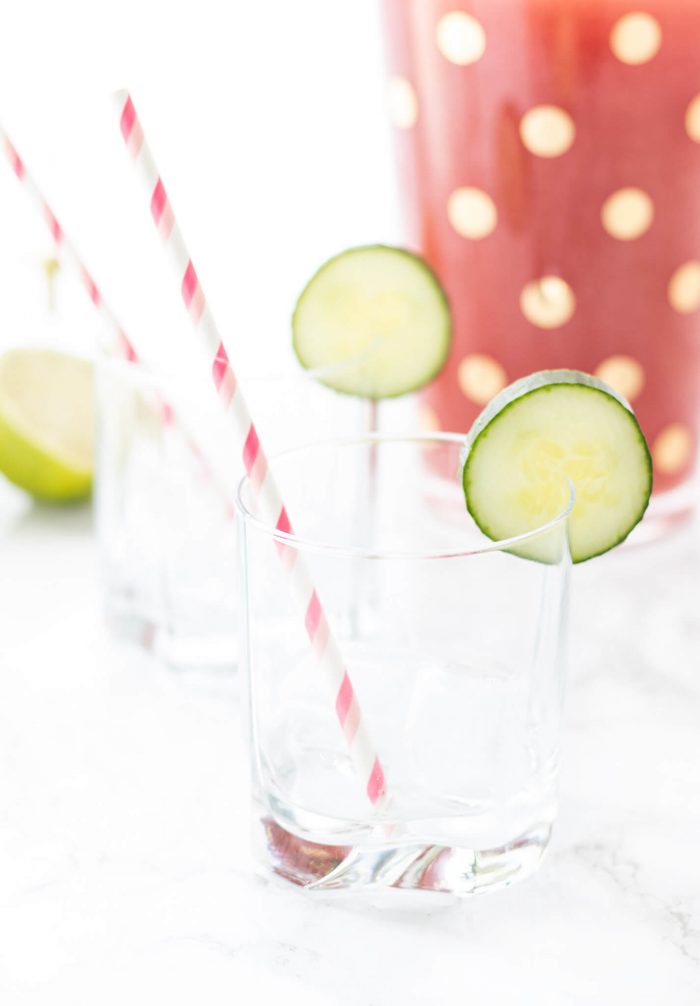 Empty glass with striped white and pink straw and a cucumber