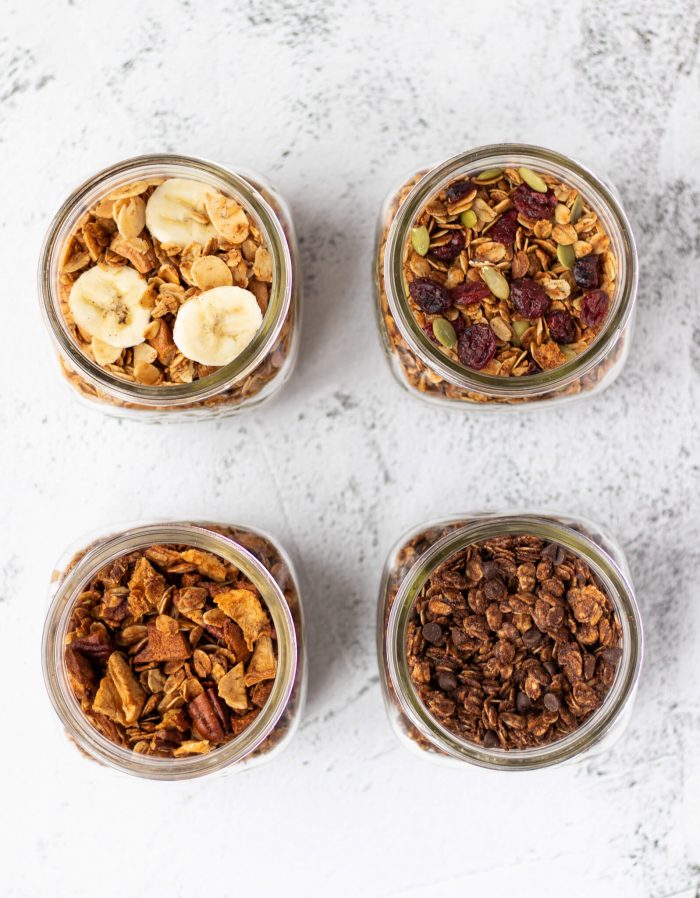 Jars filled with four different types of granola: Banana nut, Cranberry pumpkin seed, apple pecan, and double chocolate