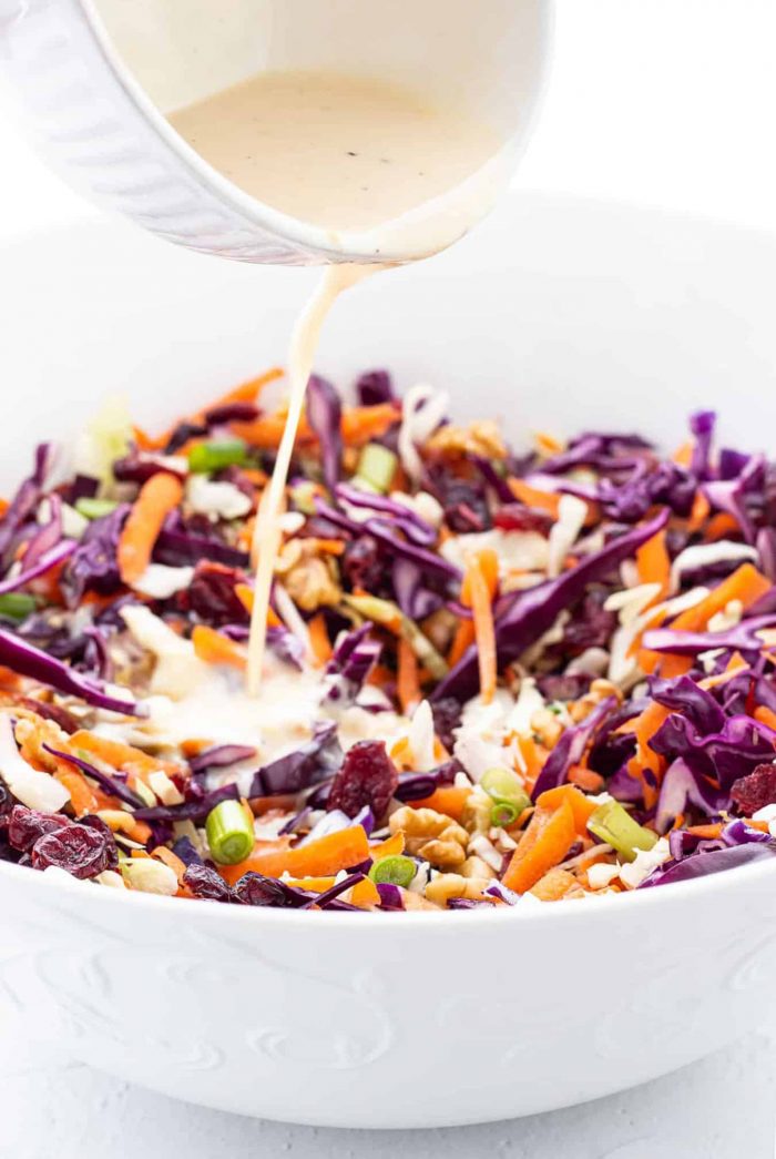 pouring creamy dressing into bowl of coleslaw