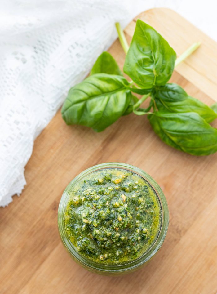 Overhead shot of pesto in a jar next to fresh basil leaves.