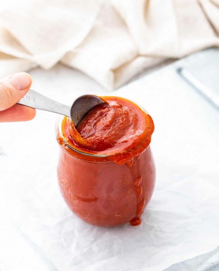 A spoon in a jar of BBQ sauce with sauce dripping out of jar