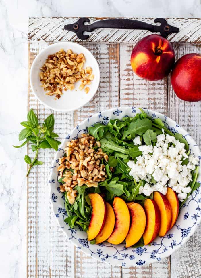 sliced nectarines, crumbled feta and chopped walnuts on a bed of arugula with nectarines. walnuts and fresh basil beside