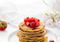 stack of pancakes topped with diced strawberries with strawberries and flowers in background