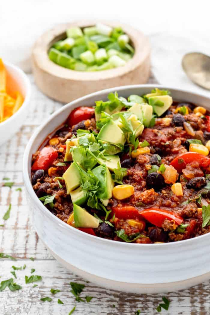 close up of bowl of beef and quinoa chili with diced avocado and cilantro