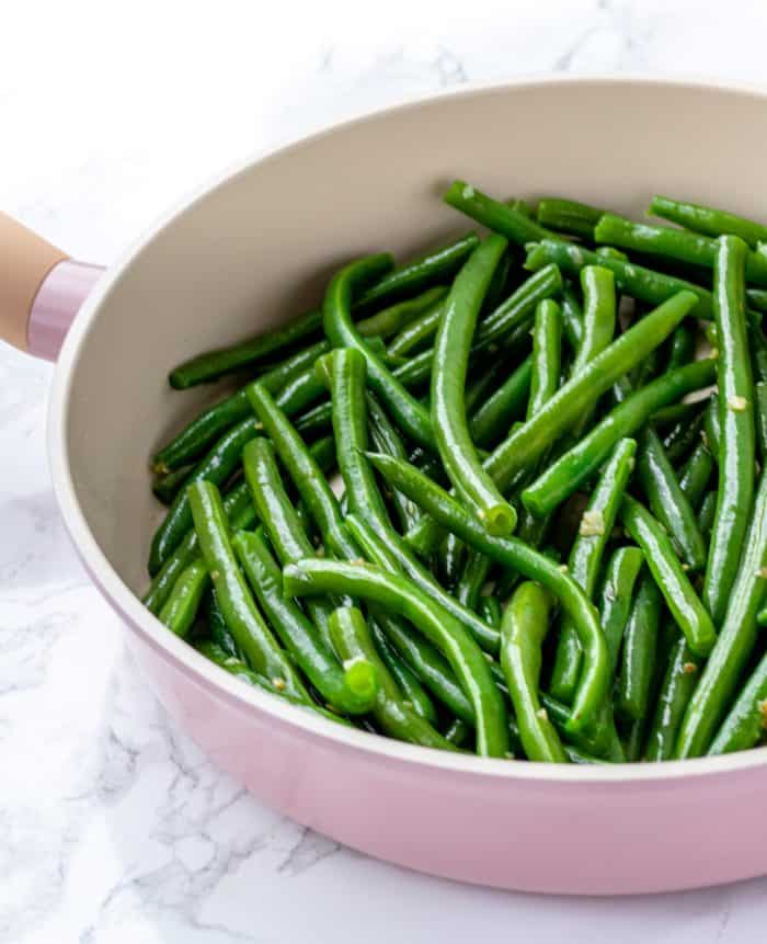 green beans with garlic and olive oil being sauteed in a pan