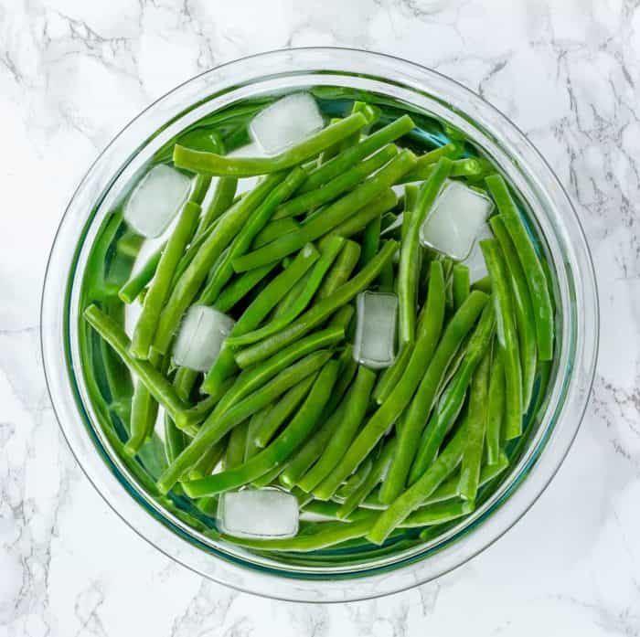 green beans chilling in bowl of ice water on marble background