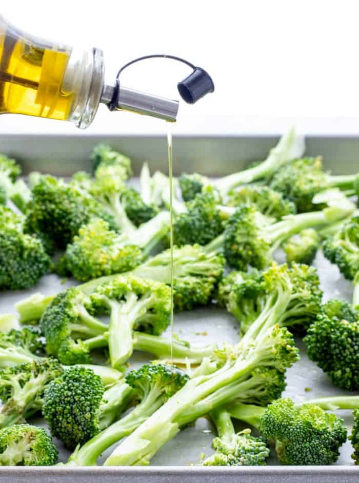 Pouring olive oil over the broccoli.