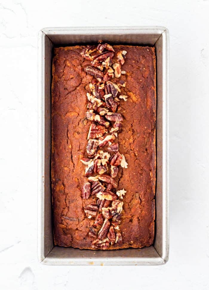 Baked pumpkin bread in a loaf pan topped with pecans