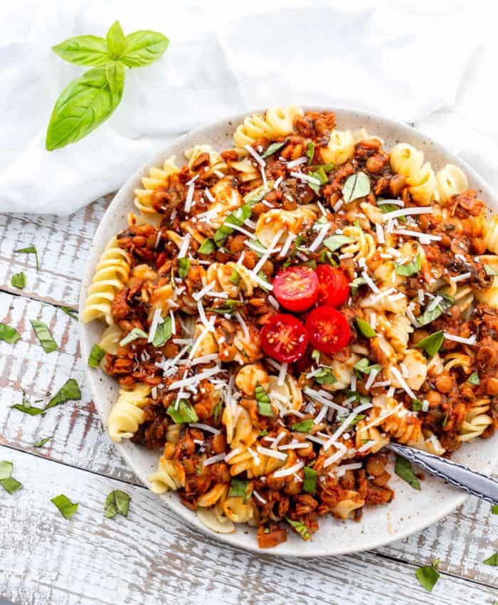Plate of lentil sauce on bed of pasta garnished with fresh basil and tomatoes with a fork