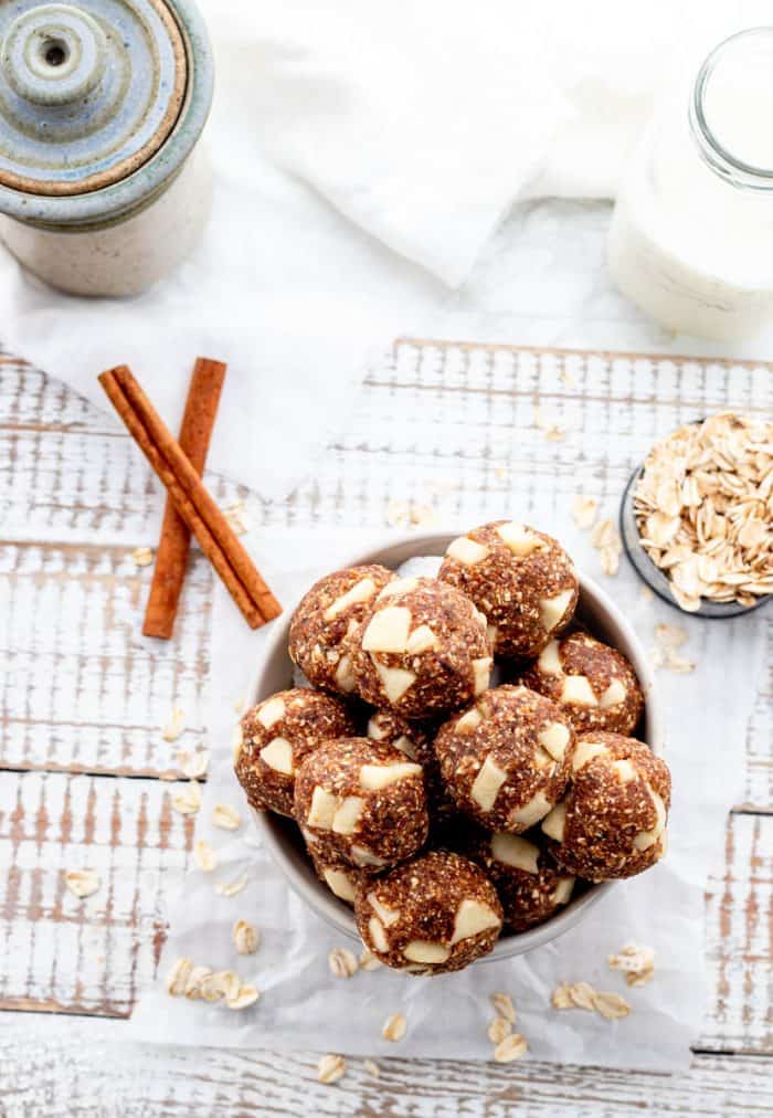 Bowl of energy balls with oats, cinnamon sticks and jug of milk on rustic white board