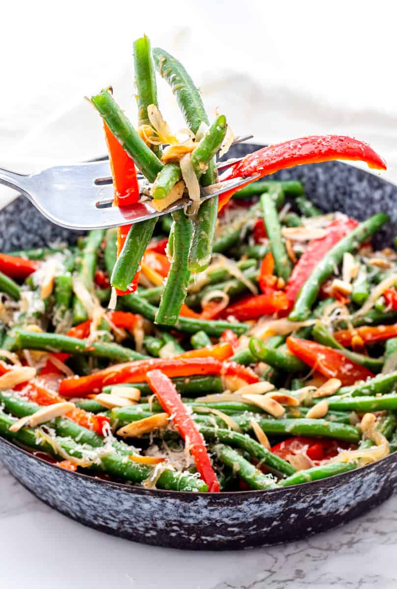 A fork picking up green beans and red pepper slices.