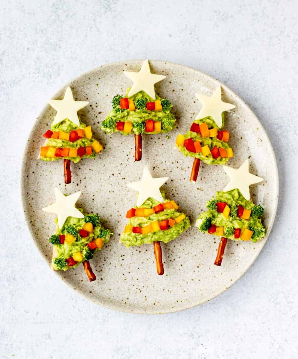 Avocado pita Christmas trees on a plate with cheese stars and pretzel trunks.
