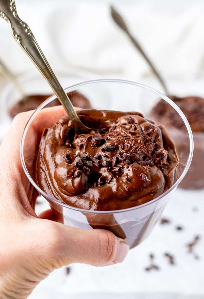 A hand holding a glass of the chocolate avocado pudding towards the camera.