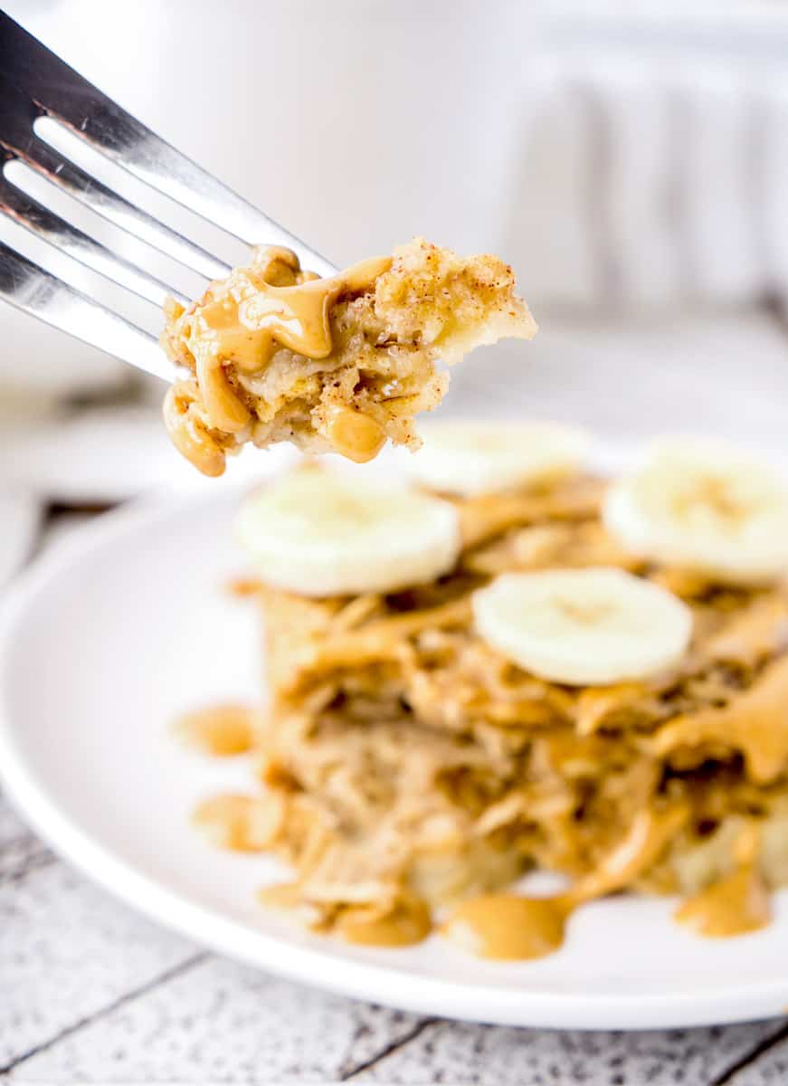 A fork holding up a piece of baked oatmeal with piece in background with banana slices