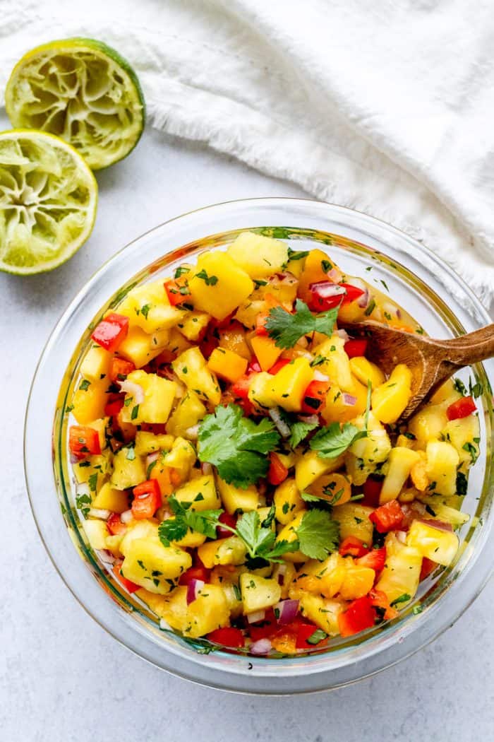 A bowl of pineapple mango salsa with a wooden spoon in it.