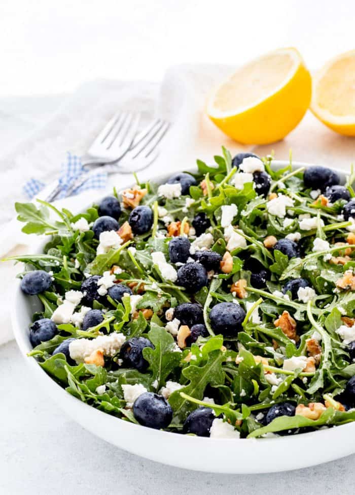 A bowl of blueberry walnut salad in front of lemon halves.