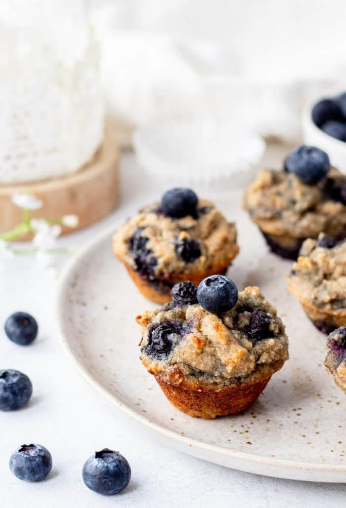 mini blueberry banana muffins on a plate next to small white flowers and fresh blueberries