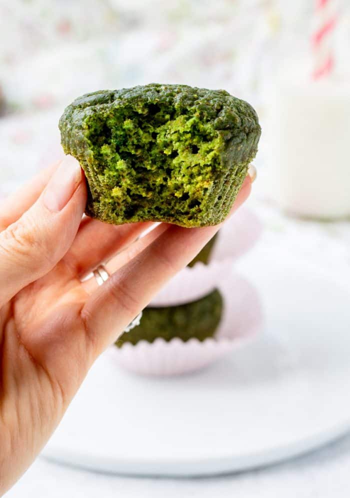 holding a spinach muffin with a bite taken out of it
