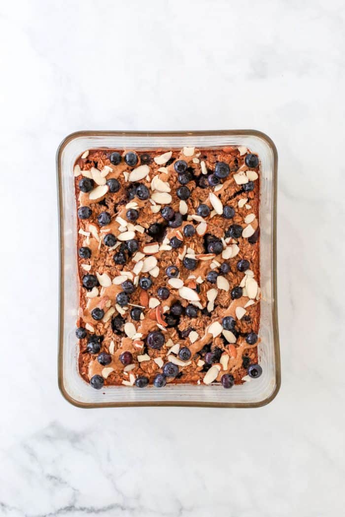 The oatmeal in a glass dish topped with fresh blueberries, sliced almonds and almond butter.