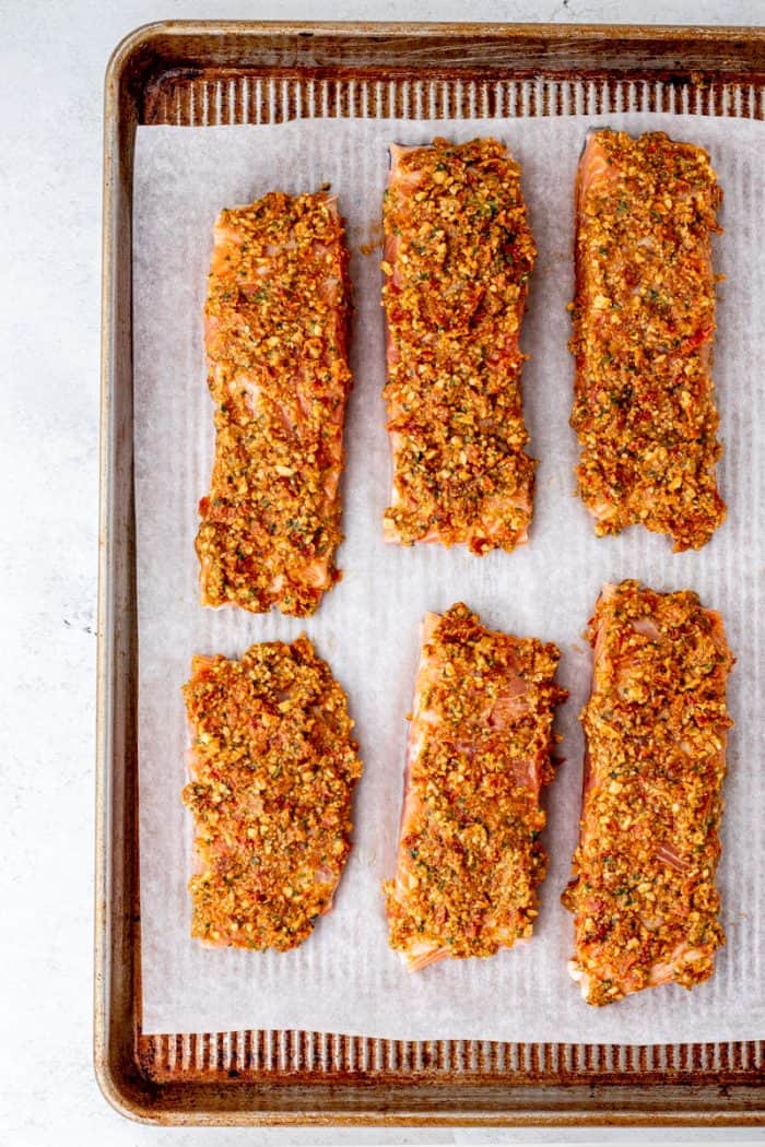 Six pesto crusted salmon fillets on a baking sheet.