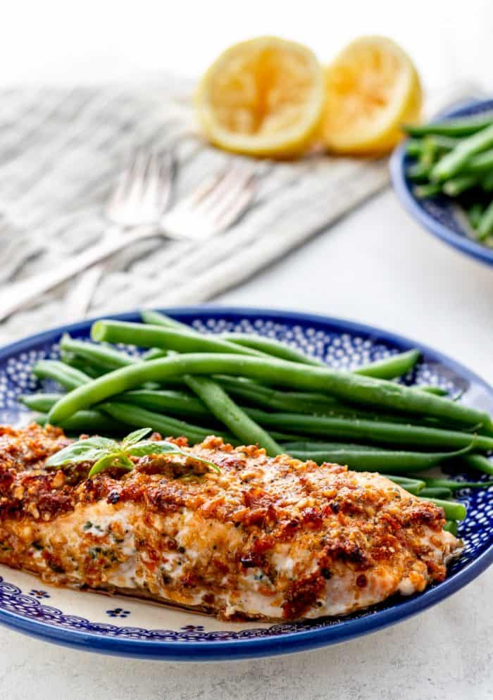 A pesto crusted salmon fillet on a plate with green beans.