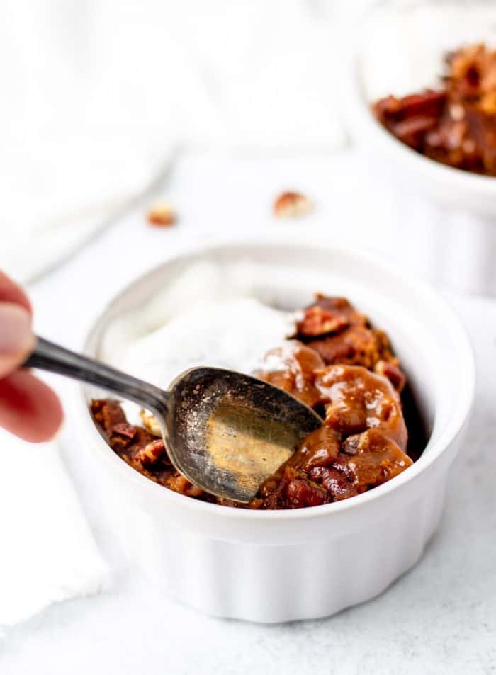Digging a spoon in pumpkin cake with pudding and pecans in a ramekin