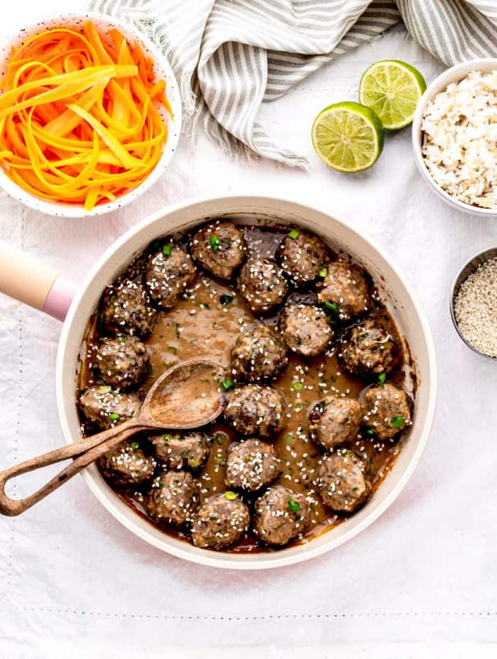 Asian meatballs and sauce in a skillet with a spoon.