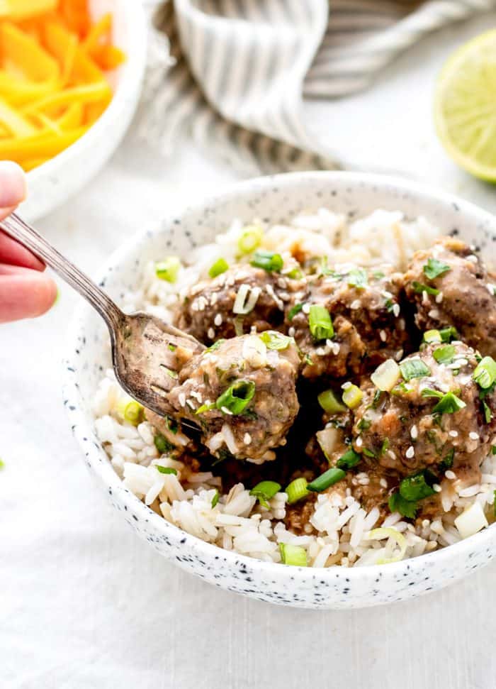A fork picking up a meatball from the bowl of rice.