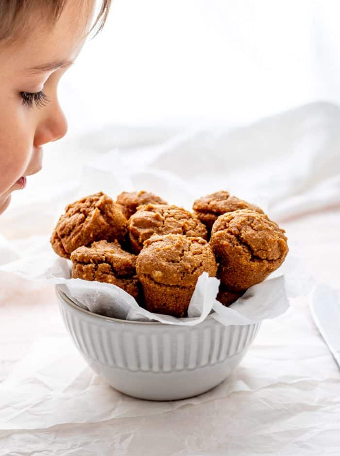 Little boy smelling small bowl full of mini muffins on parchment paper