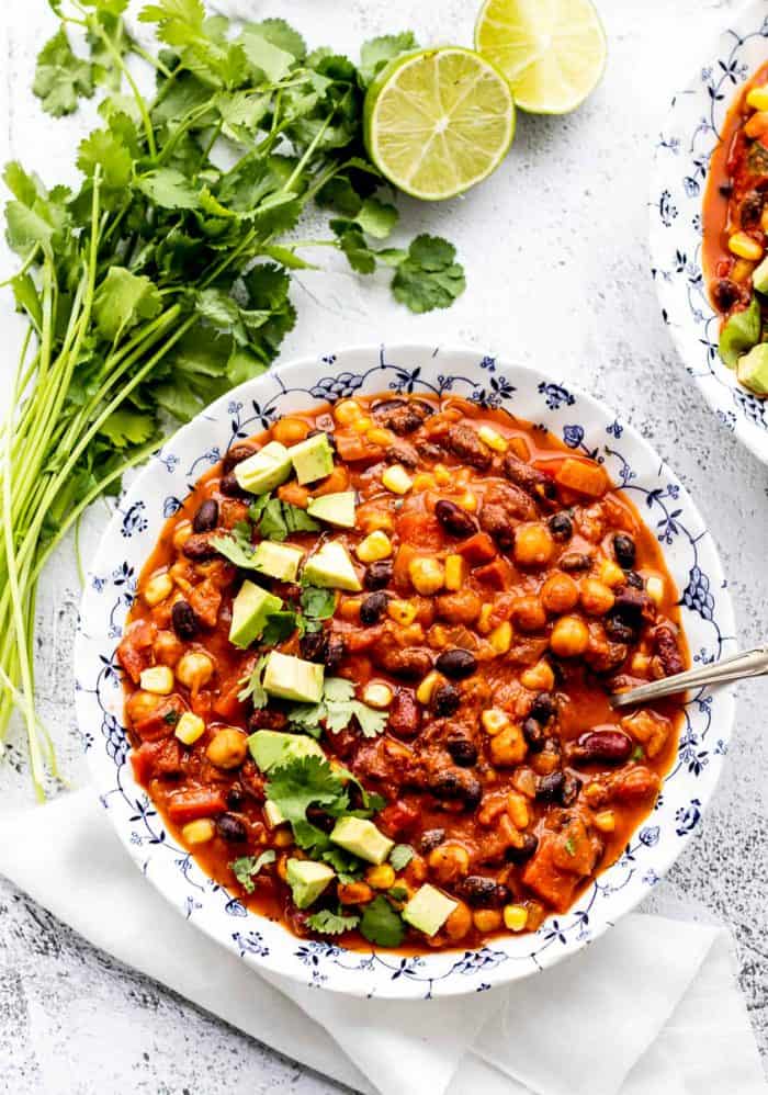 chili served in a blue and white bowl with avocado, cilantro and lime